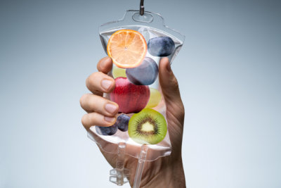 Person's Hand Holding Saline Bag Filled With Various Fruit Slices Against Grey Backdrop