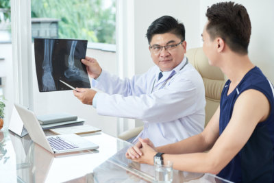 Adult Asian man in medical apparel demonstrating X-ray picture of legs