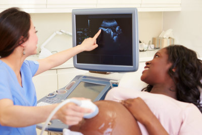 Pregnant Woman Having 4D Ultrasound Scan In Clinic With Nurse Pointing To Screen
