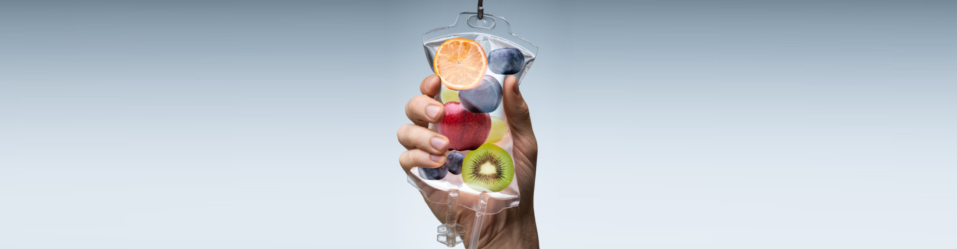 Person's Hand Holding Saline Bag Filled With Various Fruit Slices Against Grey Backdrop