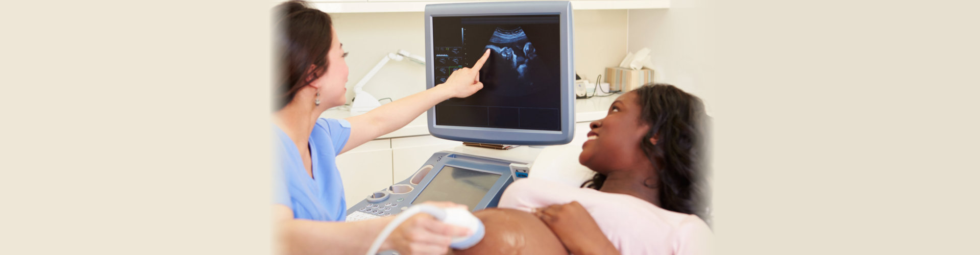 Pregnant Woman Having 4D Ultrasound Scan In Clinic With Nurse Pointing To Screen