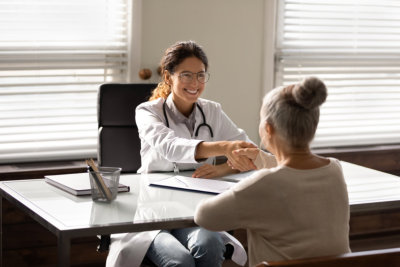 Smiling young hispanic female doctor shake hand of elderly woman patient