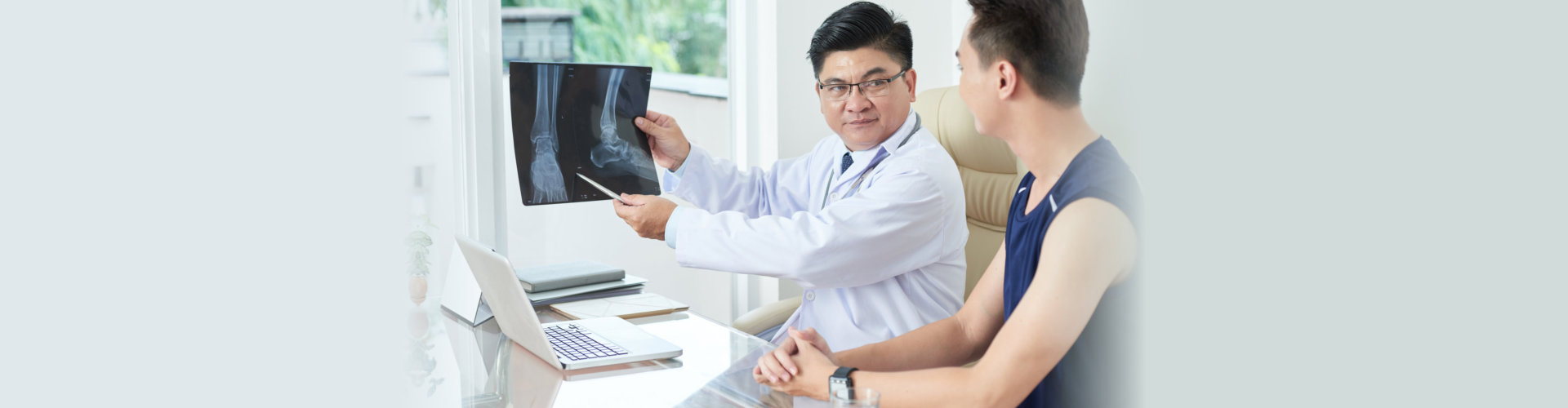 Adult Asian man in medical apparel demonstrating X-ray picture of legs