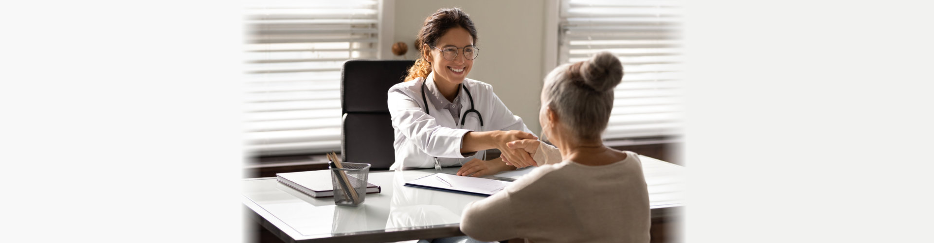 Smiling young hispanic female doctor shake hand of elderly woman patient